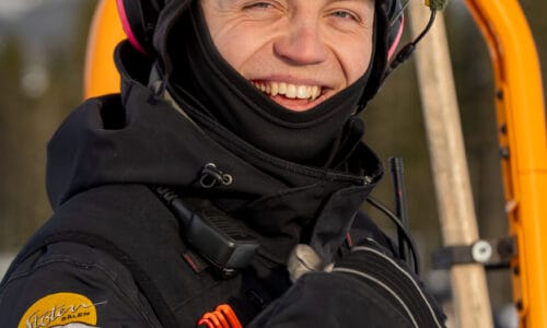 Mechanic in black uniform on snowmobile smiles at the camera.