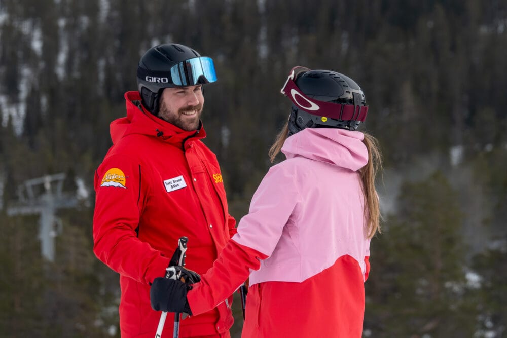 Ski instructor in red uniform giving a private lesson to a woman in a pink jacket.