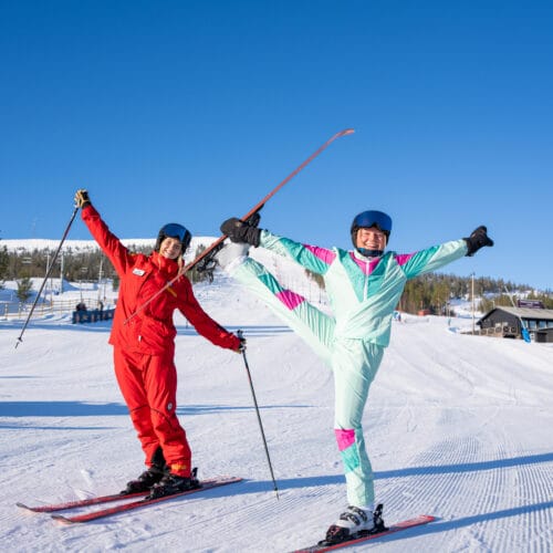 People in colourful clothes on a ski slope performing ski ballet.