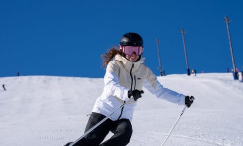 Skiers in white jackets swinging down a sunny piste with a clear blue sky in the background.
