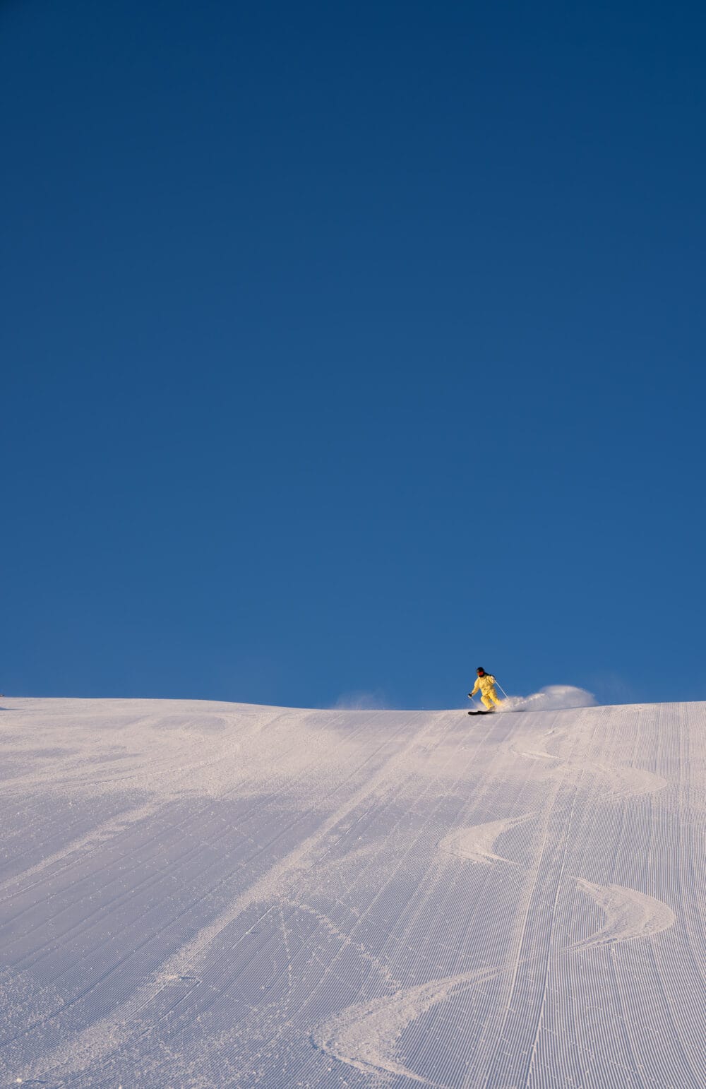 Skidåkare i gul dräkt på solig pist med klar blå himmel ovanför.