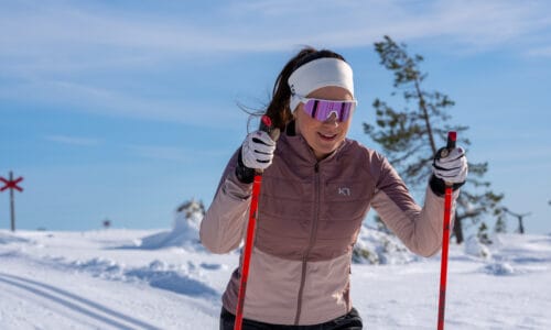 Person åker längdskidor med stavar i snötäckt landskap och klarblå himmel.
